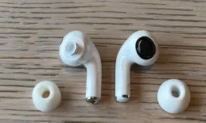 Dwa białe słuchawki AirPods i dwie gumowe nakładki na drewnianym tle.