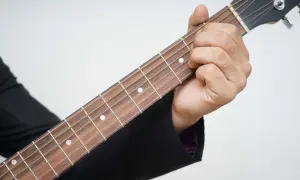 Dłoń dociska struny gitary, tworząc akord. Piękna muzyka na gitarę w zasięgu ręki.