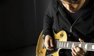 Młody gitarzysta z kostką w dłoni pokazuje, jak trzymać kostkę od gitary, grając na złotej gitarze elektrycznej.