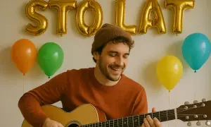 Uśmiechnięty mężczyzna w czapce gra na gitarze na tle złotych balonów z napisem "STO LAT" i kolorowych balonów.