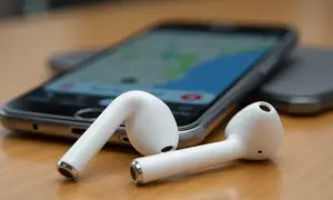 Białe słuchawki AirPods leżące obok telefonu z mapą na ekranie.
