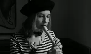 Kobieta w beretce gra na flecie. Pokazuje, jak się gra gamę na flecie, skupiona na melodii.
