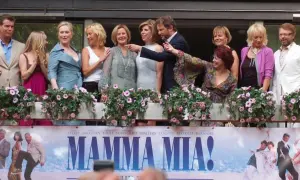 Obsada filmu "Mamma Mia!" pozdrawia fanów. W tle plakat z bohaterami, przypominający o wesołych piosenkach z filmu.