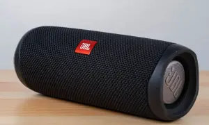 Czarny głośnik JBL Flip leży na drewnianym blacie. Dowiedz się, jak włączyć słuchawki bezprzewodowe JBL, by cieszyć się muzyką.