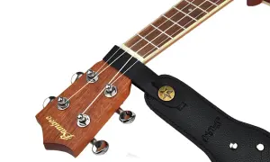 Czarny pasek do gitary przymocowany do gryfu ukulele. Pokazuje, jak przyczepić pasek do gitary, zaczepiając go o główkę instrumentu.