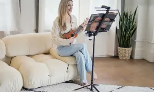 Uśmiechnięta kobieta gra na ukulele, korzystając z podstawki do nut.