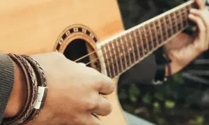 Dłoń z bransoletką gra na gitarze, tworząc dźwięki w tonacji c-dur.