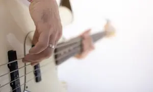 Dłoń z pierścionkiem ćwiczy naukę gry na gitarze basowej, szarpiąc struny.