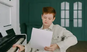 Chłopiec z rudymi włosami ćwiczy grę na pianinie, studiując nuty. Może właśnie poznaje nazwy oktaw, przygotowując się do występu.