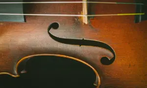 Drewniany korpus skrzypiec z widocznymi strunami. Delikatne rysy na lakierze świadczą o historii instrumentu, który czeka na swoje dźwięki.
