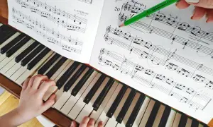 Dziecko uczy się grać proste melodie na pianino. Zielony ołówek wskazuje nuty w zeszycie.
