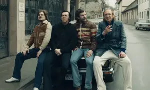 Czterech mężczyzn w stylu lat 70. siedzi na samochodzie. Jeden z nich pali papierosa, przypominając scenę z filmu "Jak pokochałam gangstera".