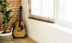 Akordy gitara klasyczna, instrument oparty o ceglaną ścianę, obok doniczki z rośliną.