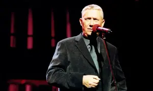 Mężczyzna w eleganckim garniturze śpiewa na scenie. Jego piosenka młynarskiego porusza serca publiczności.
