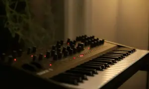 Ciemny, nowoczesny elektroniczny instrument klawiszowy z wieloma pokrętłami i czerwonymi diodami.