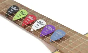 Kolorowe kostki do gry na gitarze Alice leżą na strunach. Każda kostka ma inny kolor i grubość, gotowa do tworzenia muzyki.