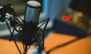 Profesjonalny mikrofon studyjny na statywie, idealny do podcastów. W tle widać sprzęt audio.