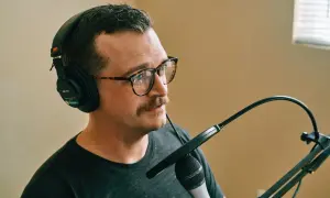 Mężczyzna w okularach i słuchawkach przygotowuje się do nagrywania mikrofonu.