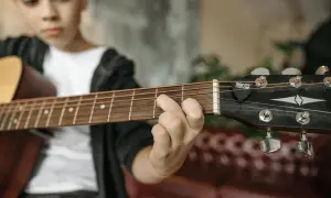 Chłopiec ćwiczy akord d7 na gitarze. Palce układają się na gryfie, gotowe do zagrania kolejnej nuty.