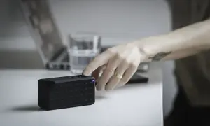 Ręka naciska przycisk na czarnym głośniku JBL, przygotowując go do połączenia z komputerem.