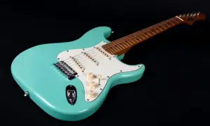 Turkusowa gitara elektryczna, idealna do nauki jak grać na gitarze elektrycznej. Ma biały pickguard i drewnianą podstrunnicę.