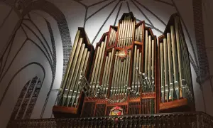 Majestatyczny utwór na organy w kościele, z rzędami złotych piszczałek i ozdobnym detalem na środku.