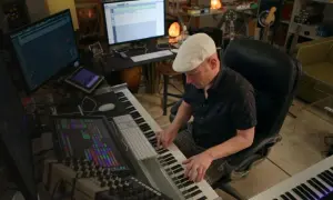 Muzyk w białej czapce tworzy muzykę w studiu. Komputery, klawiatury i miksery sugerują, że zastanawia się, dlaczego nie soundtrack.