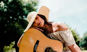 Kobieta w kapeluszu opiera się o gitarę, marząc o najpiękniejszych piosenkach na gitarę.
