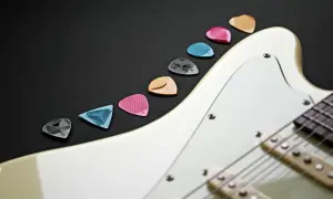 Kolorowe kostki do gitary ułożone wzdłuż białego korpusu instrumentu. Idealne akcesoria, by zacząć naukę gry na gitarze.