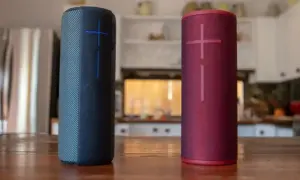 Dwa głośniki JBL, niebieski i czerwony, stoją na drewnianym stole. Dowiedz się, jak podłączyć głośnik JBL z telefonem.