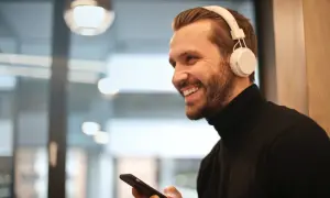 Uśmiechnięty mężczyzna w słuchawkach JBL trzyma telefon, zastanawiając się, jak podłączyć słuchawki JBL do telefonu.