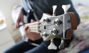 Osoba gra na gitarze basowej, wydobywając głębokie dźwięki na basie.