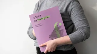 Osoba trzyma okładkę "Szkoła na fortepian Klechniowska" z grafiką fortepianu.