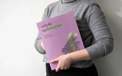 Osoba trzyma okładkę "Szkoła na fortepian Klechniowska" z grafiką fortepianu.