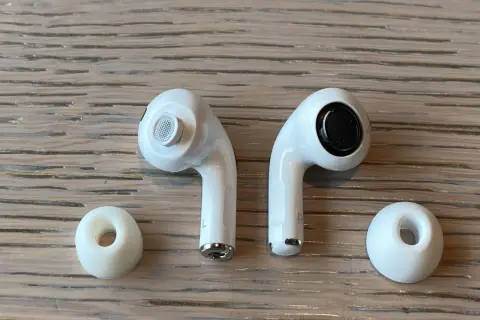 Dwa białe słuchawki AirPods i dwie gumowe nakładki na drewnianym tle.