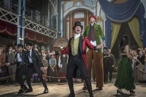 Król rozrywki, P.T. Barnum, w cyrkowym stroju wita publiczność. W tle widzimy jego artystów i widzów.