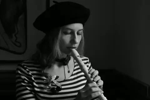 Kobieta w beretce gra na flecie. Pokazuje, jak się gra gamę na flecie, skupiona na melodii.