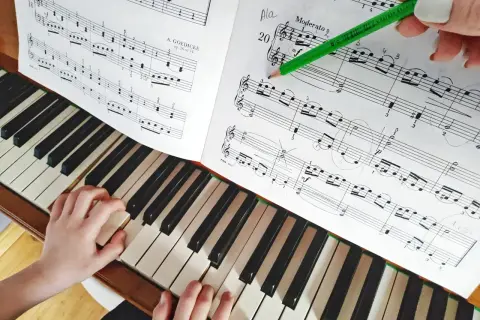 Dziecko gra proste nuty na pianino. Nauczycielka zaznacza ołówkiem fragment utworu.
