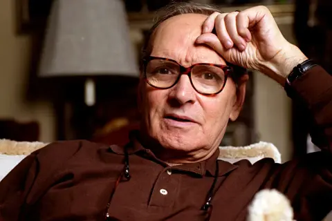 Ennio Morricone, genius kompozytor muzyki do **ennio morricone filmy**, zamyślony z ręką na czole.