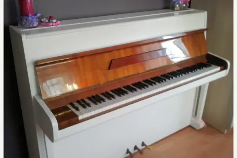 Białe pianino z drewnianymi elementami. Zastanawiasz się, ile kosztuje strojenie pianina?