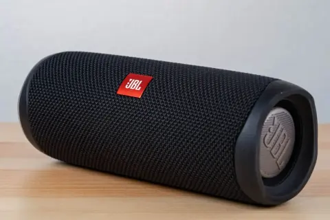 Czarny głośnik JBL Flip leży na drewnianym blacie. Dowiedz się, jak włączyć słuchawki bezprzewodowe JBL, by cieszyć się muzyką.