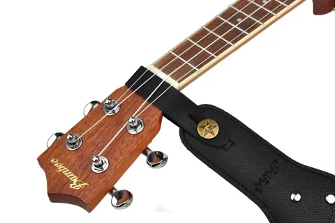 Czarny pasek do gitary przymocowany do gryfu ukulele. Pokazuje, jak przyczepić pasek do gitary, zaczepiając go o główkę instrumentu.