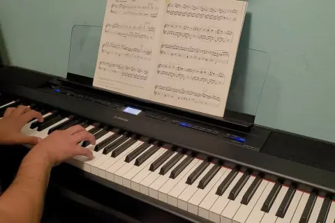 Palce pianisty tańczą po klawiszach, tworząc melodię. Nuty na pulpicie wskazują drogę.
