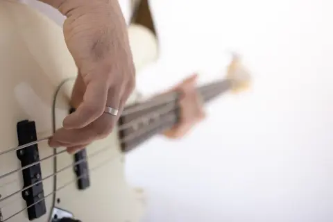Dłoń z pierścionkiem ćwiczy naukę gry na gitarze basowej, szarpiąc struny.