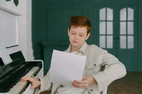 Chłopiec z rudymi włosami ćwiczy grę na pianinie, studiując nuty. Może właśnie poznaje nazwy oktaw, przygotowując się do występu.