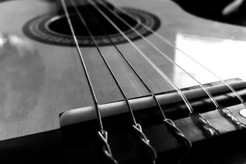 Zbliżenie na gitarę, gdzie widoczne są napięte struny. Ich metaliczny połysk i sposób mocowania przy mostku sugerują gotowość do wydobycia pięknych dźwięków.