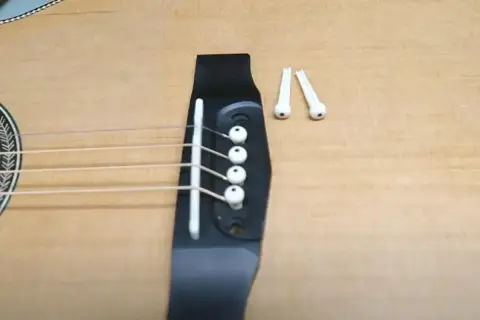 Jak zmienić struny w gitarze klasycznej? Widok na mostek gitary z naciągniętymi strunami i dwoma wyjętymi kołeczkami.