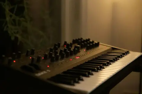 Ciemny, nowoczesny elektroniczny instrument klawiszowy z wieloma pokrętłami i czerwonymi diodami.