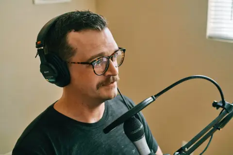 Mężczyzna w okularach i słuchawkach przygotowuje się do nagrywania mikrofonu.
