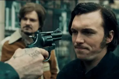 Scena z filmu, gdzie gangster celuje z rewolweru. Może to być moment z "Jak pokochałam gangstera", pełen napięcia i niepewności.